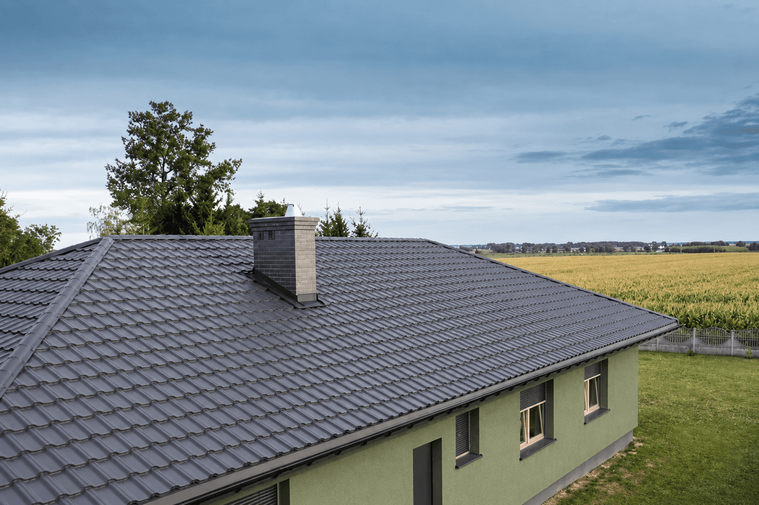 Broad graphite hipped roof on a single-storey house beside open farmland, seen from above the ridge