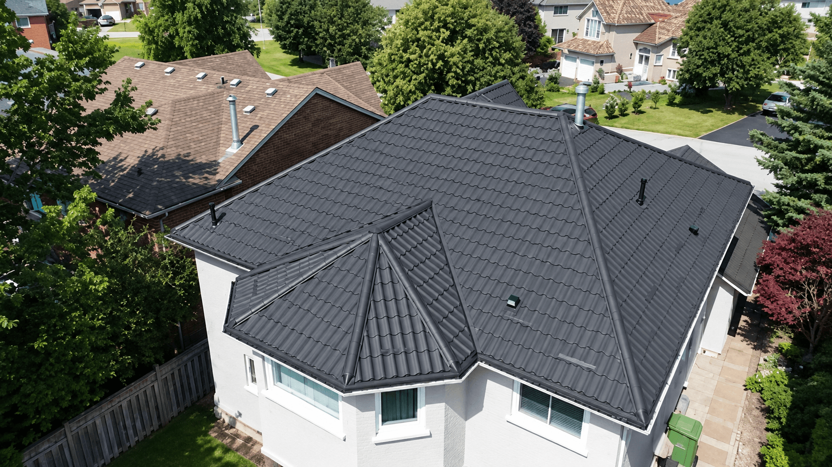 Faceted charcoal metal tile roof turning over a bay window, above white painted brick, seen from above