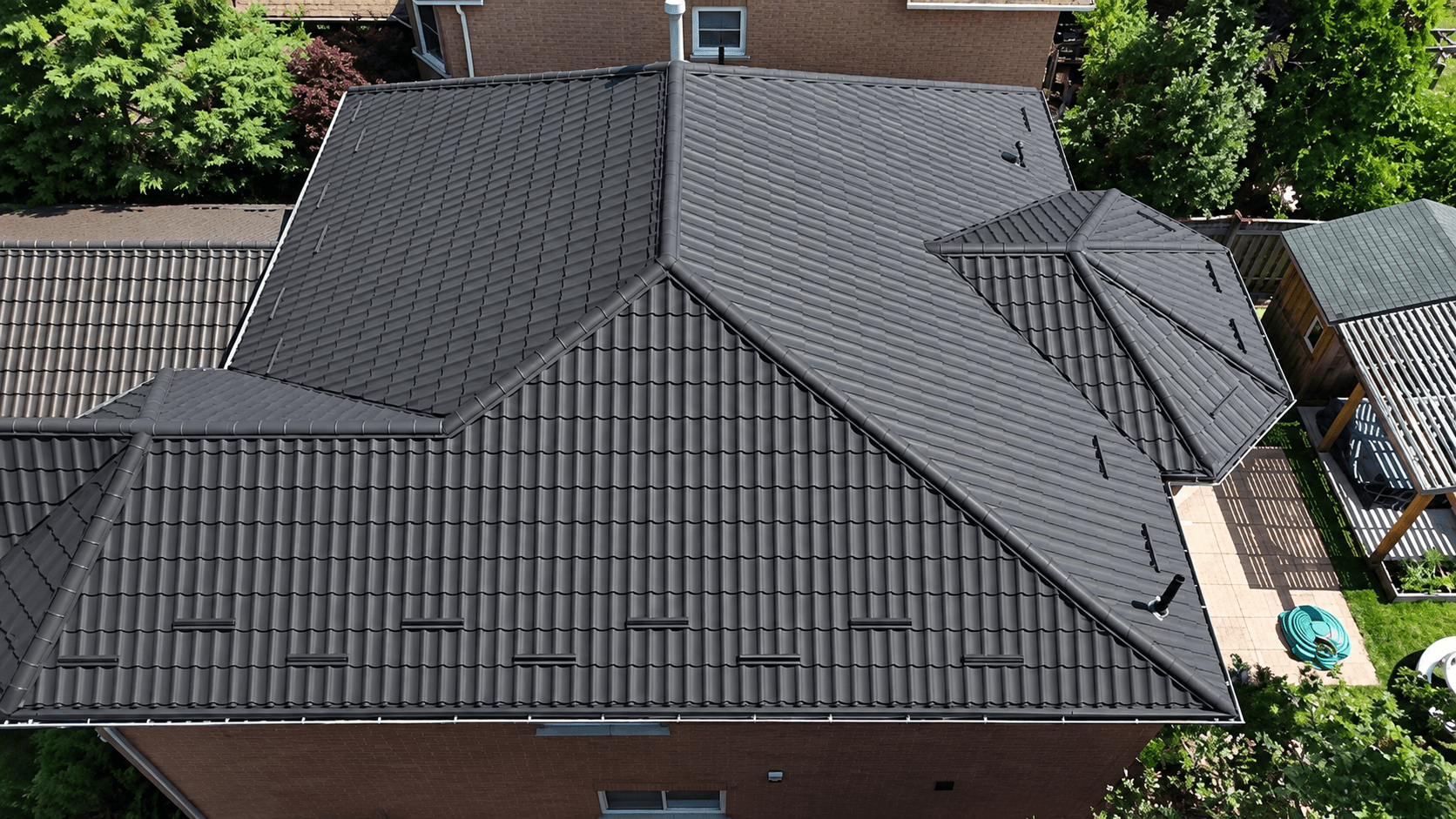 Large graphite metal tile hipped roof with valleys and a faceted bay, photographed almost in plan